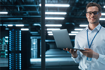 Man holding a laptop in a large server room